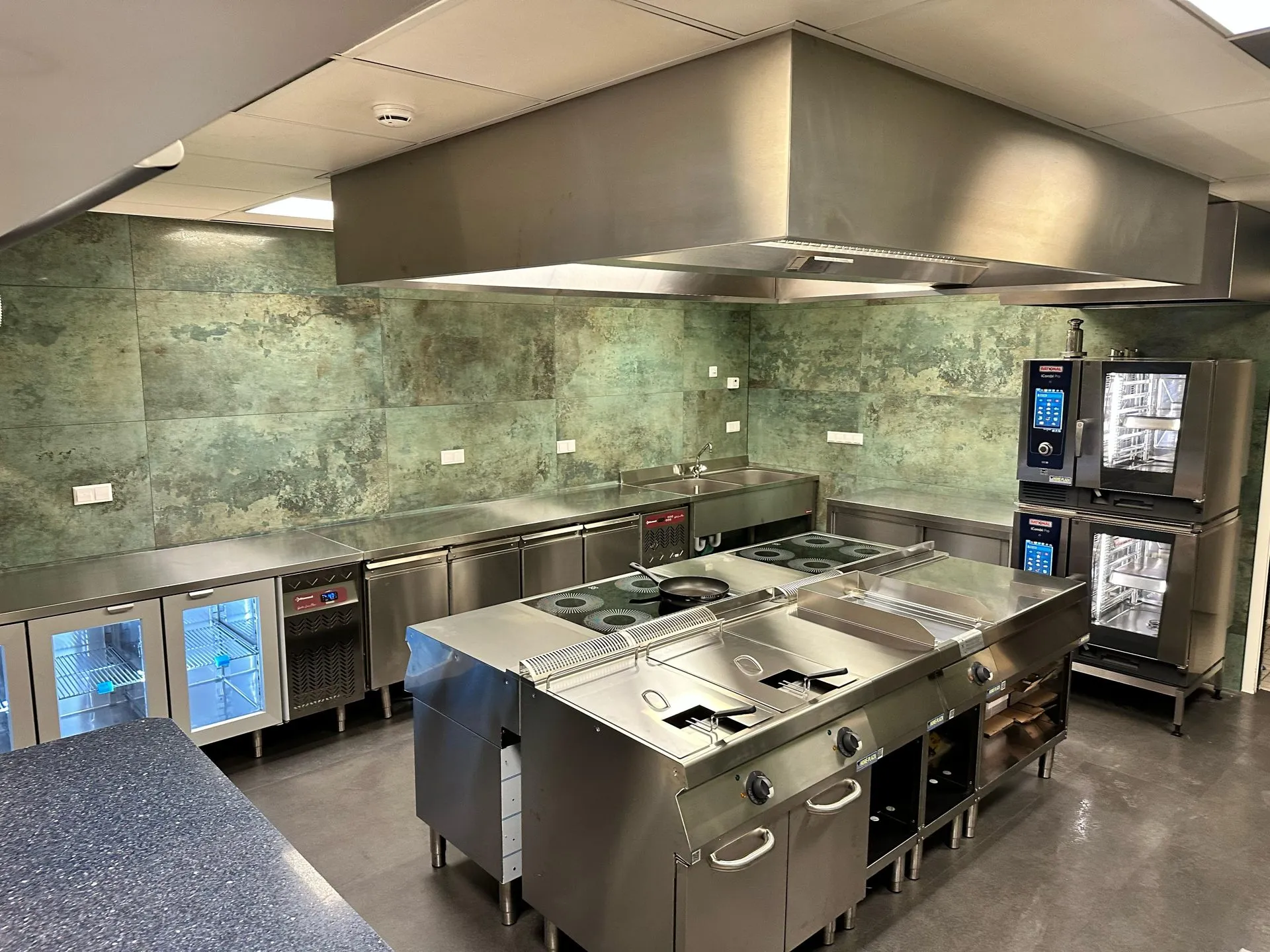 Professionele keuken bij KOCO met kookeiland, RVS-afzuigkap en combisteamers